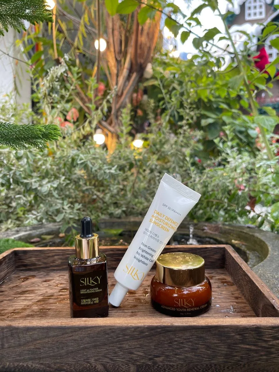 SILKY serum, sunscreen and face cream together on a wooden tray in a garden